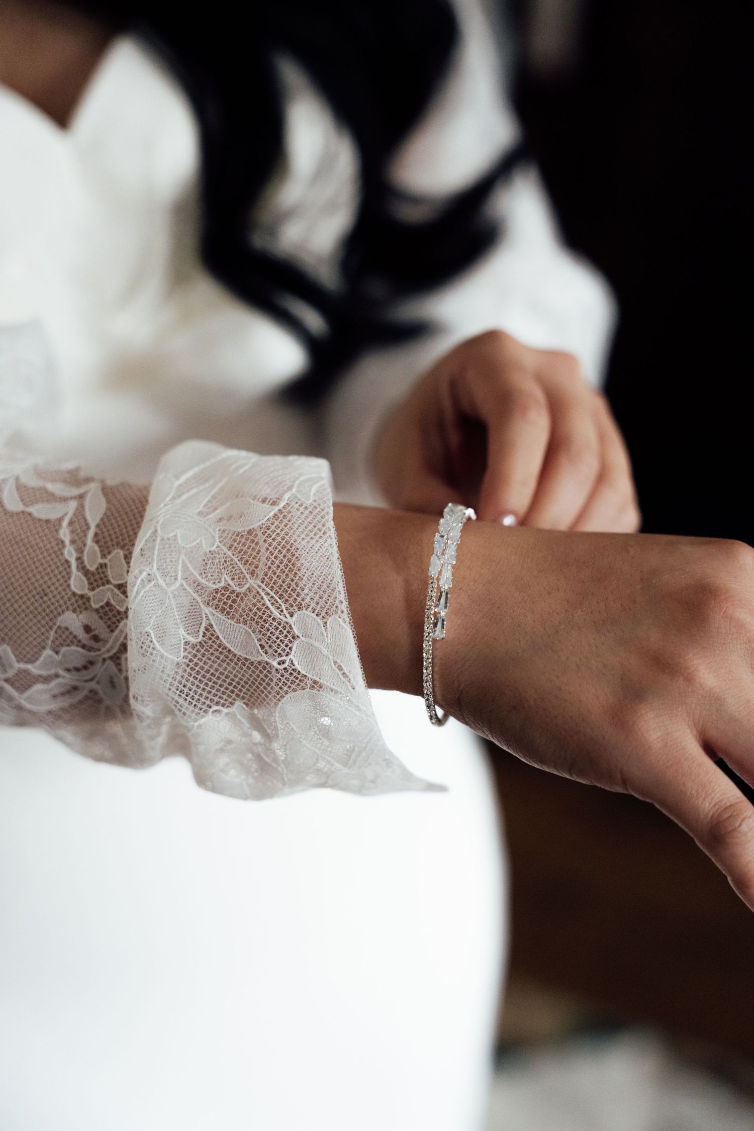 Bride wearing a diamond tennis bracelet with elegant lace wedding dress sleeve detail.