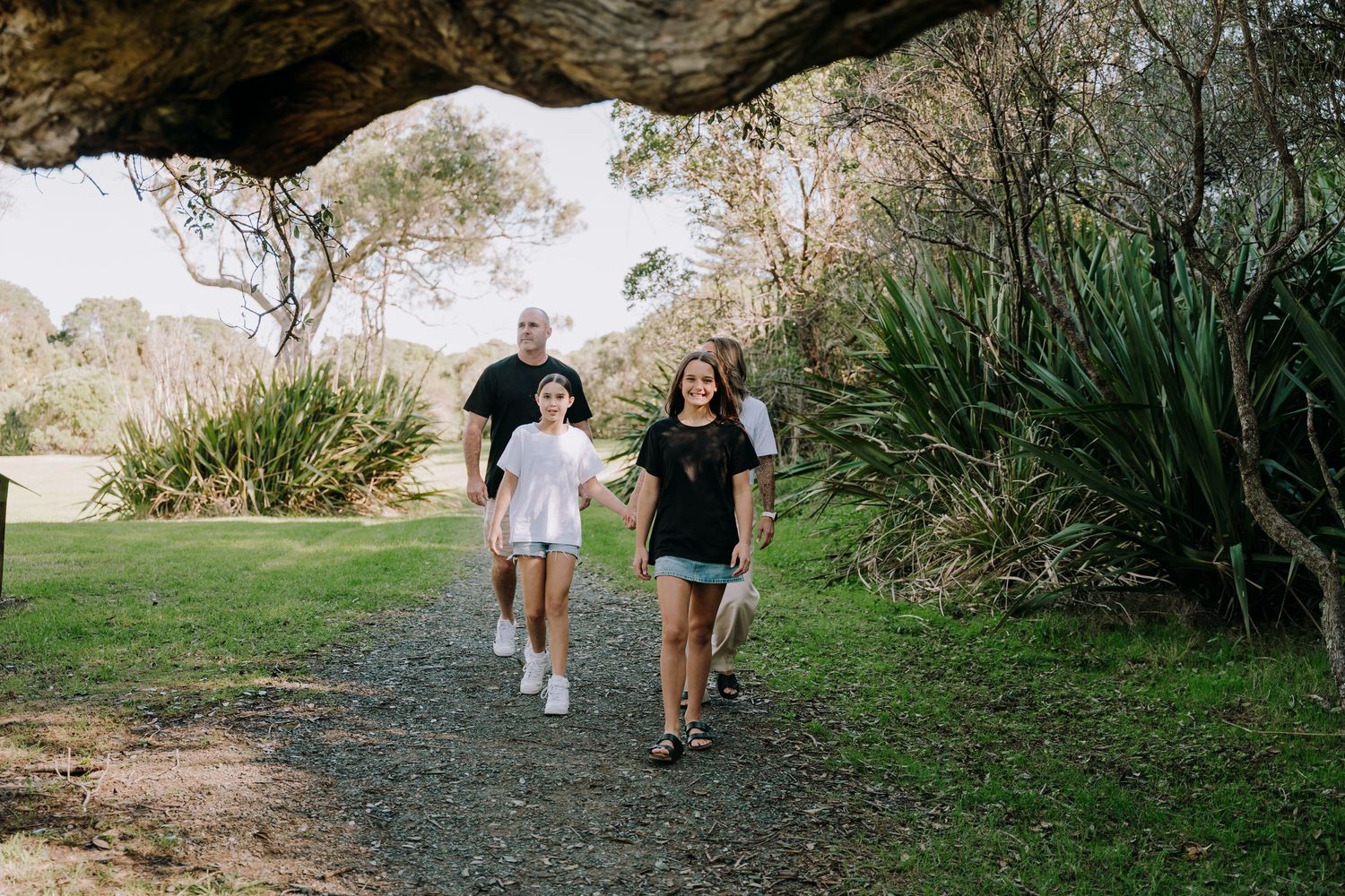 People walking together on a nature trail through lush green vegetation and trees on a sunny afternoon.