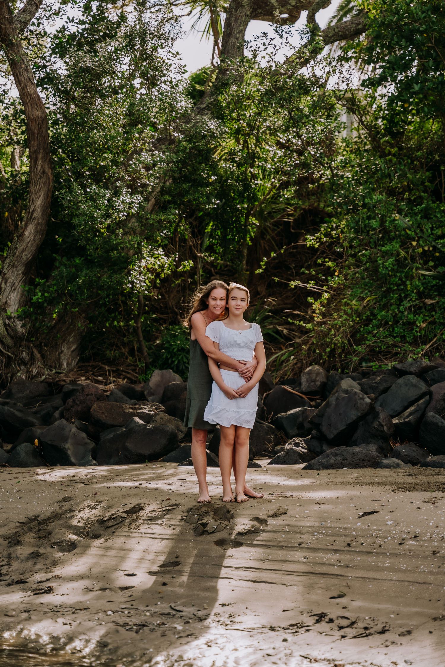 People enjoying a peaceful moment together on a secluded beach with volcanic rocks and trees.