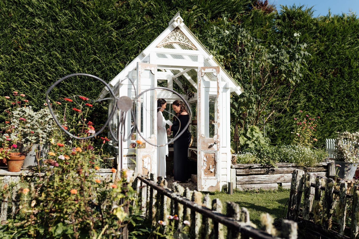 Couple sharing a romantic moment inside a charming white wooden garden gazebo surrounded by lush greenery.