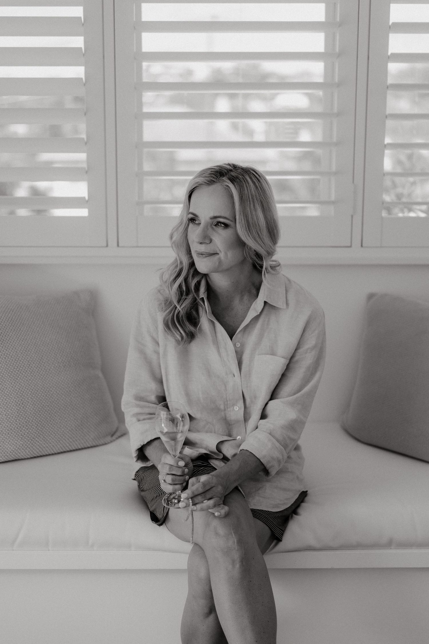 Black and white photos of woman relaxing on white couch by window with shutters.