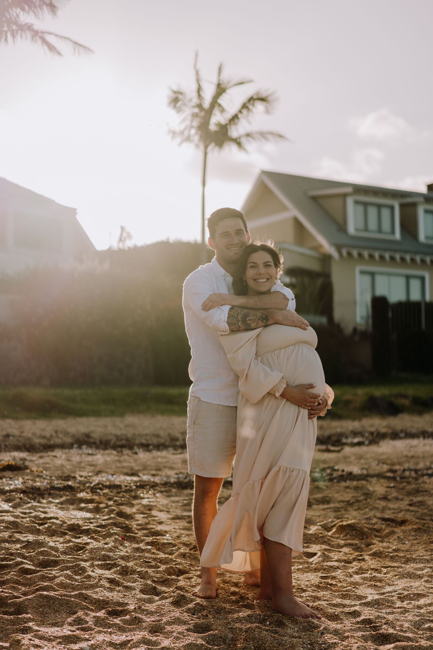 Tender embrace captured during sunset beach photoshoot with palm trees in background.