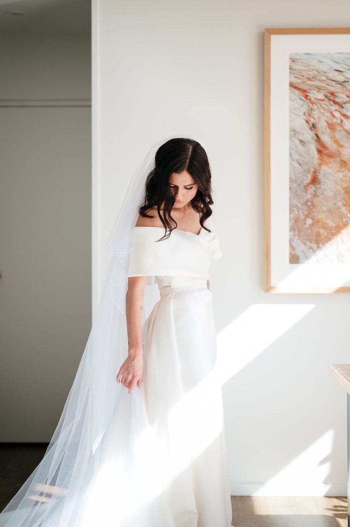 A bride in a white wedding dress stands in a sunlit room creating a series of ethereal silhouettes against a bright window.