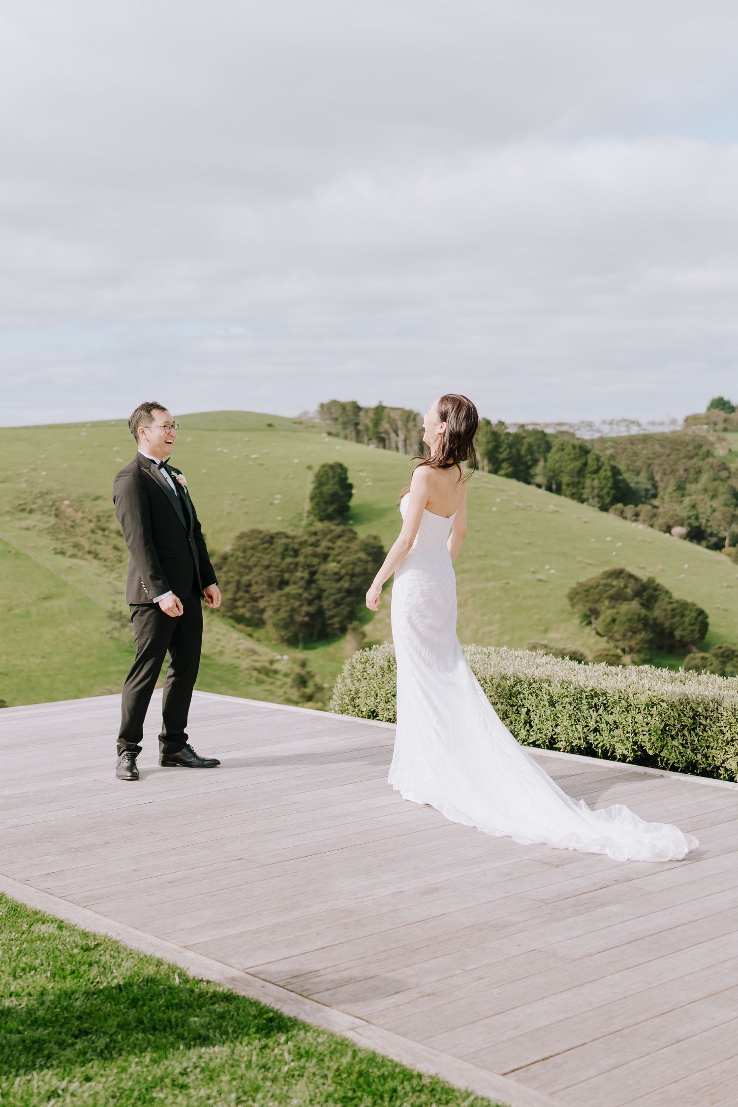 Bride and groom share first look moment on wooden deck with scenic hillside views.