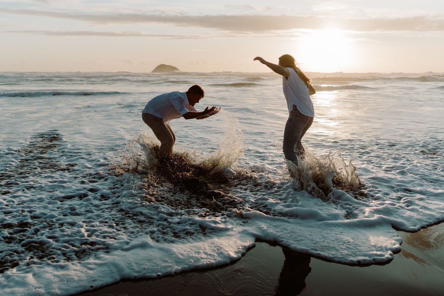Couple playing and splashing in the ocean waves during golden hour.