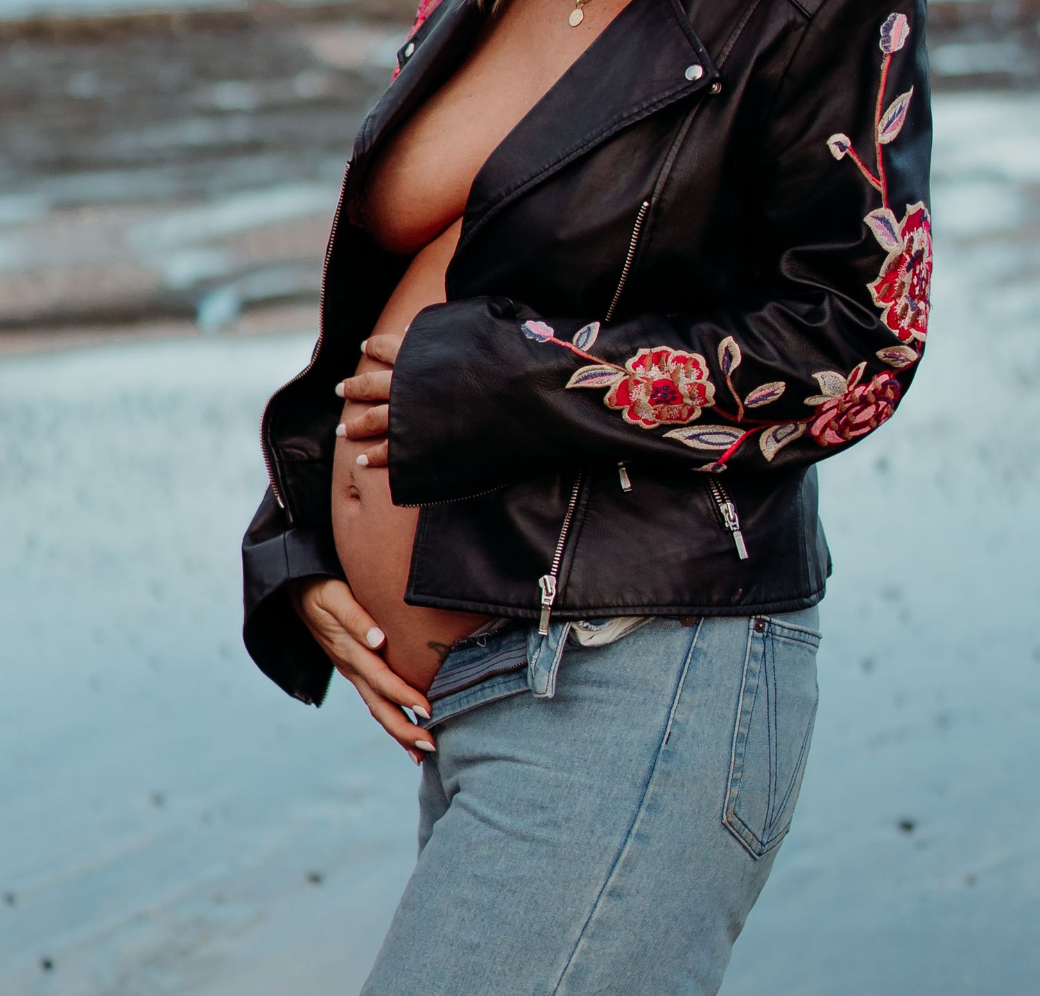 Maternity photos showing baby bump in floral black top against coastal background.