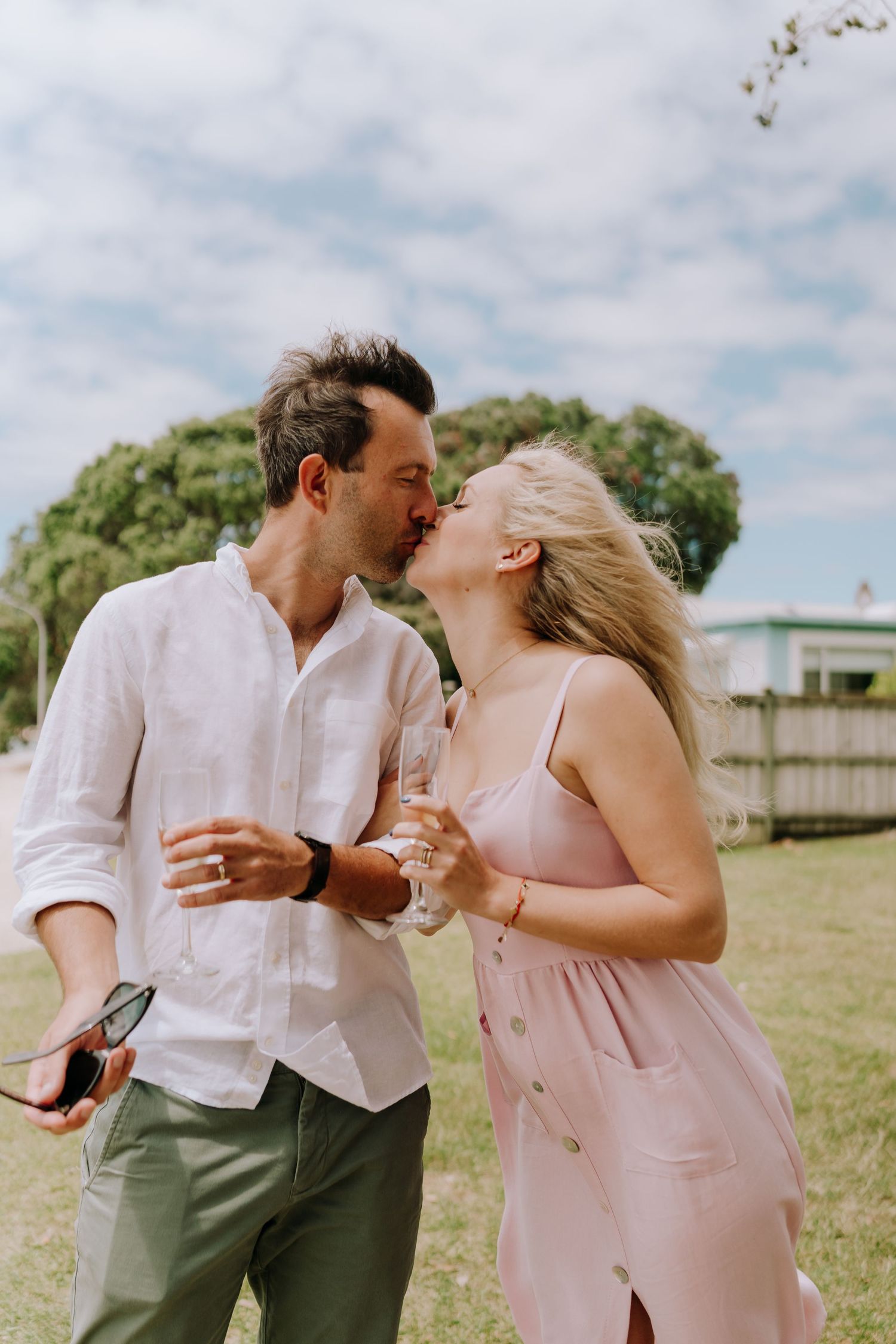 A couple in light colored outfits share joyful candid moments together in a grassy outdoor setting.