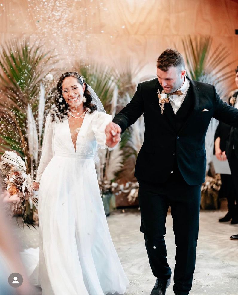A wedding couple dancing together in a ballroom with elegant decor and palm leaf decorations in the background.