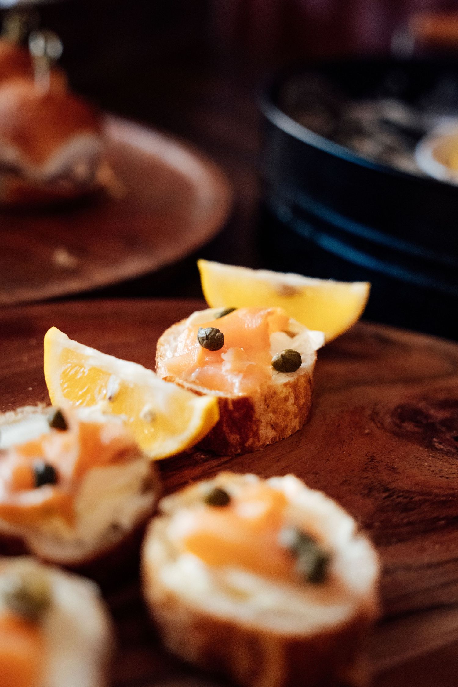 Smoked salmon crostini with capers and lemon wedges served on a rustic wooden board.