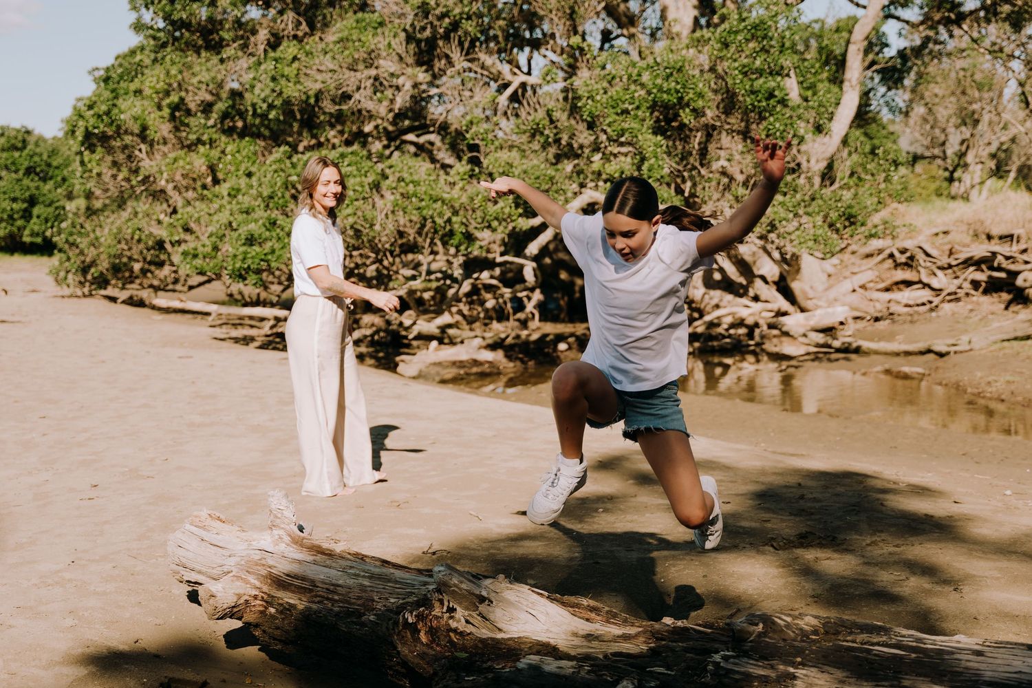A couple explores a scenic rocky beach area with lush greenery and natural formations in the background.