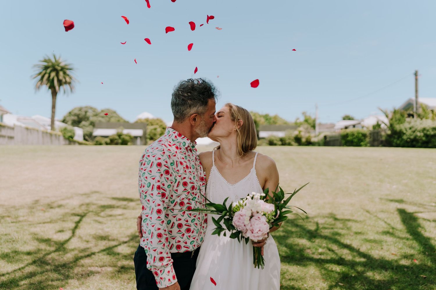 Red rose petals fall from the sky during an outdoor wedding ceremony in a desert landscape.
