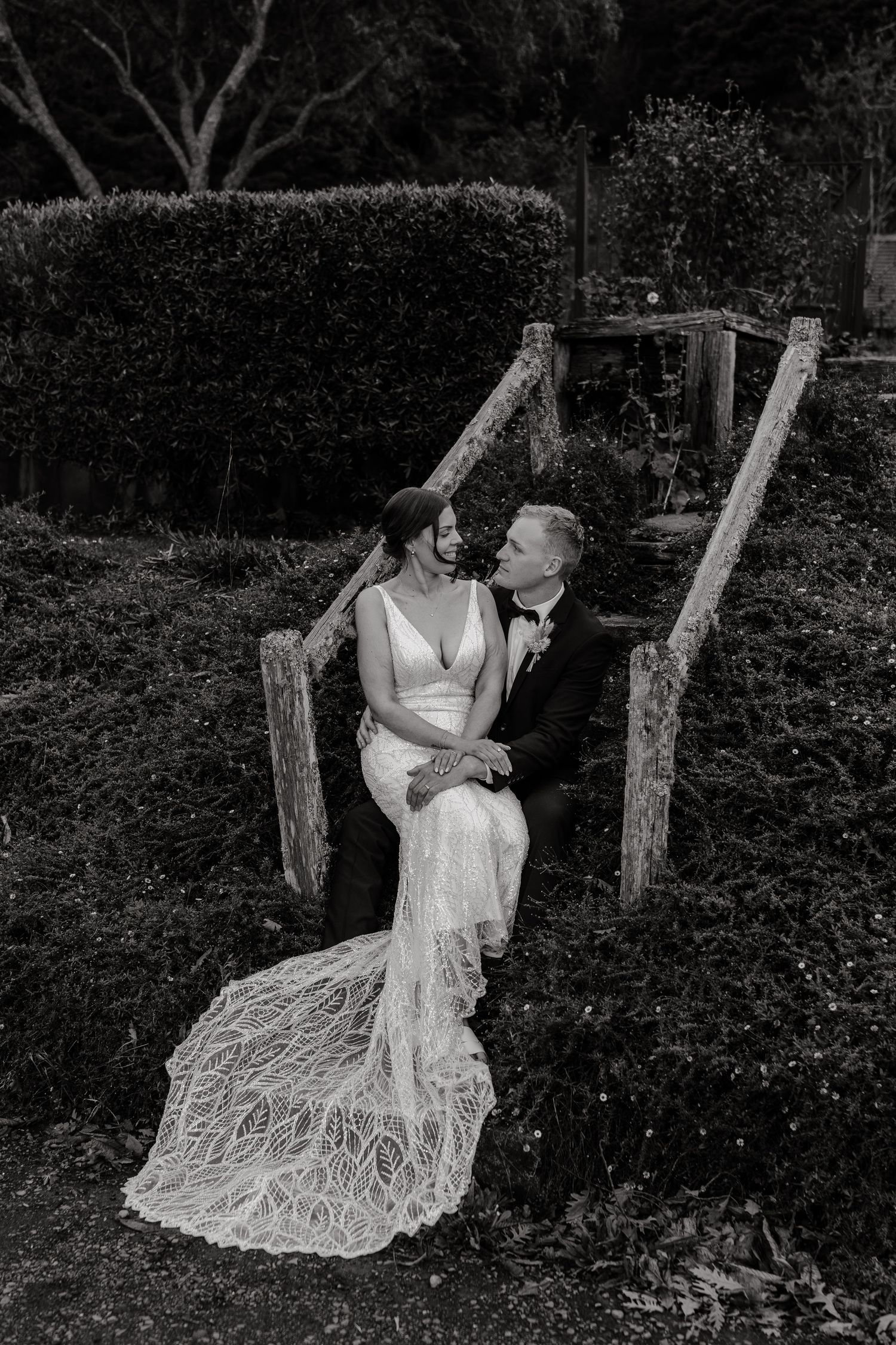 A couple in wedding attire shares romantic moments on rustic wooden swings in a lush garden setting.