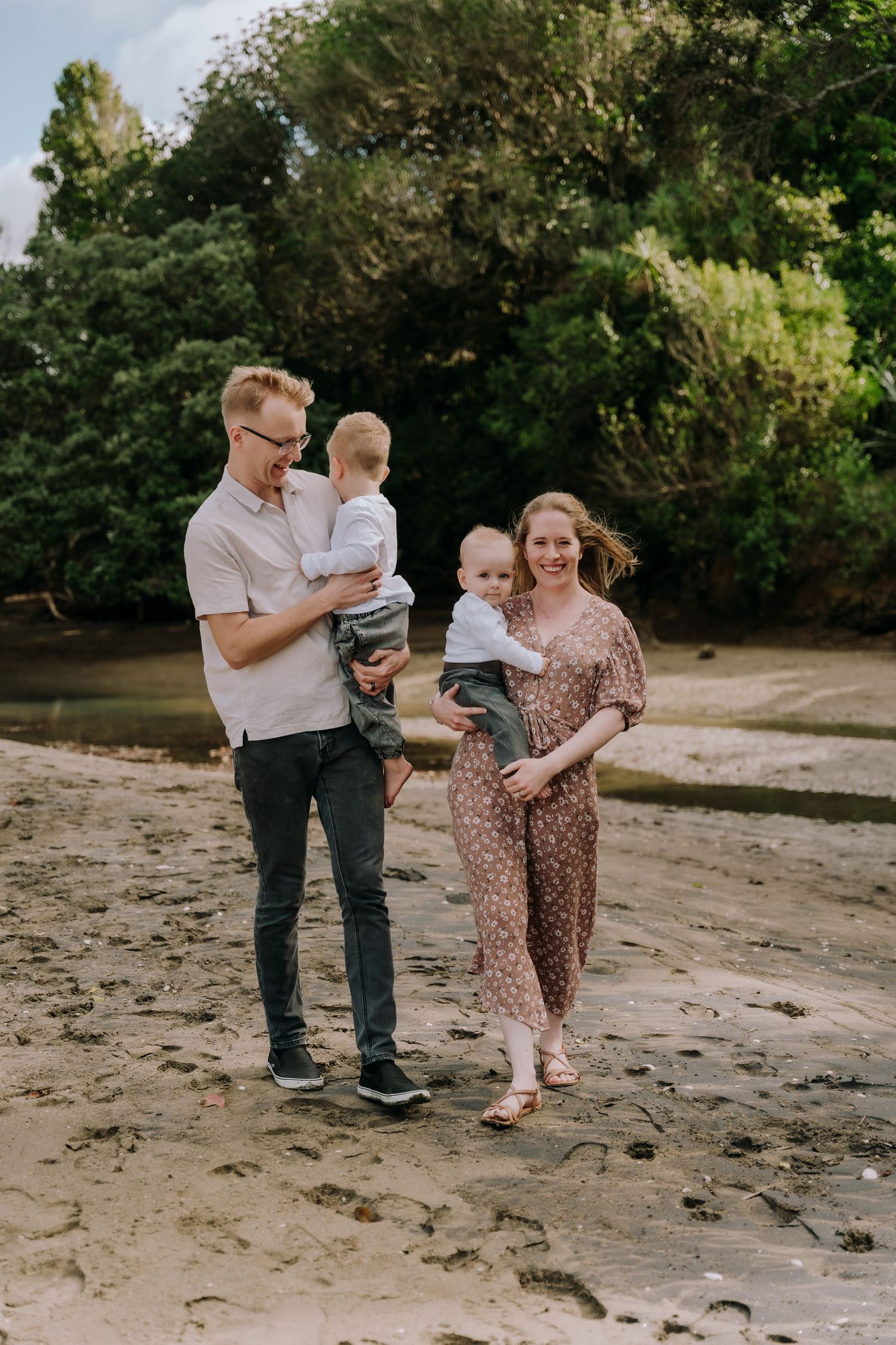 A family plays and walks together on a sandy beach surrounded by lush greenery.