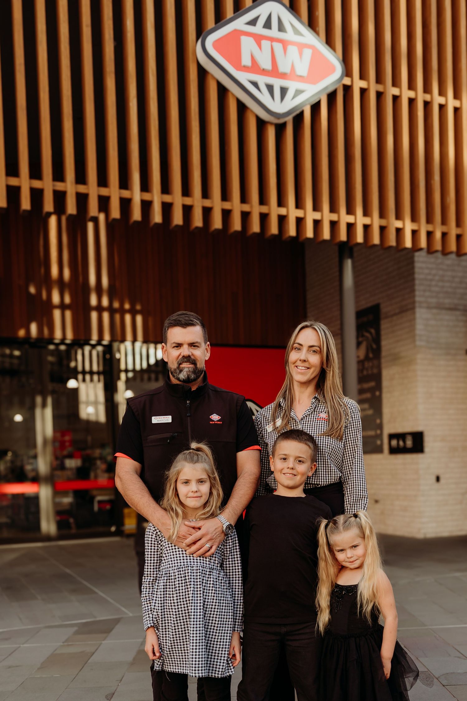 Family of five smiling together outside a New World supermarket, with parents and three young children posing for a portrait.