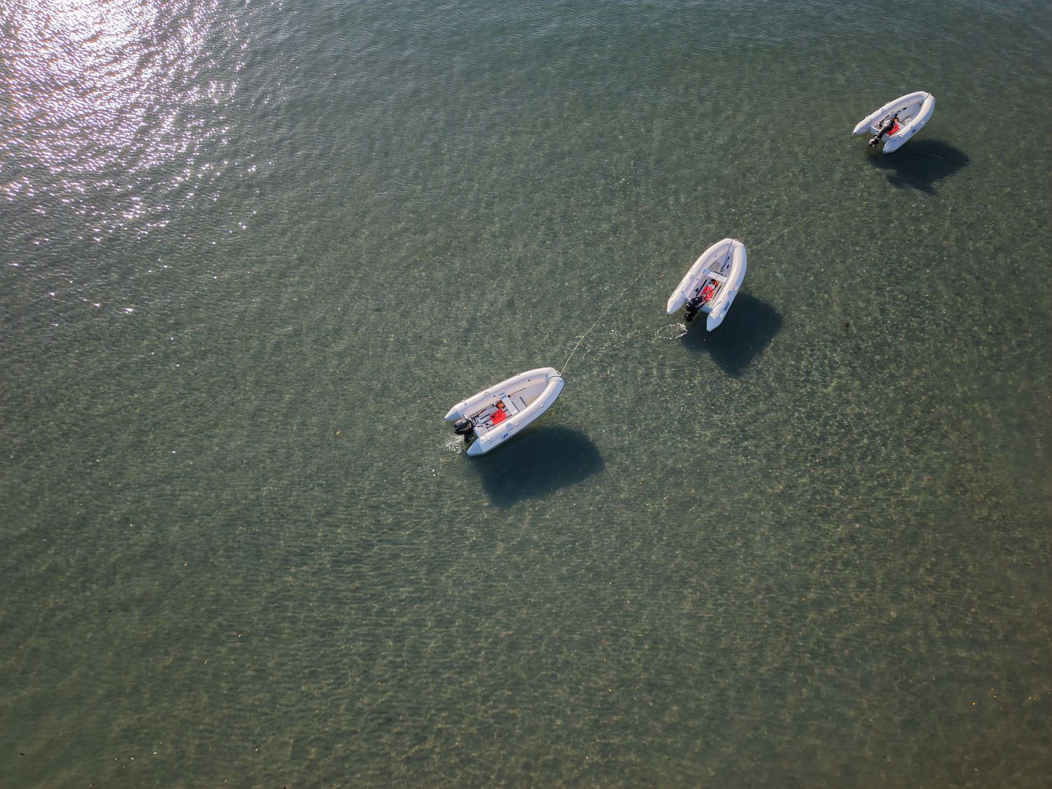 Aerial view of three white boats floating on calm green ocean water, shot from above.