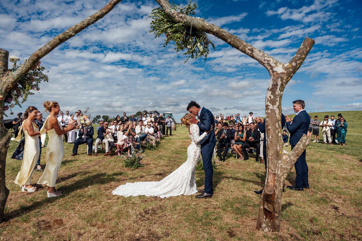 Outdoor wedding ceremony on a hilltop with bride and groom at the altar, guests seated on a sunny day.