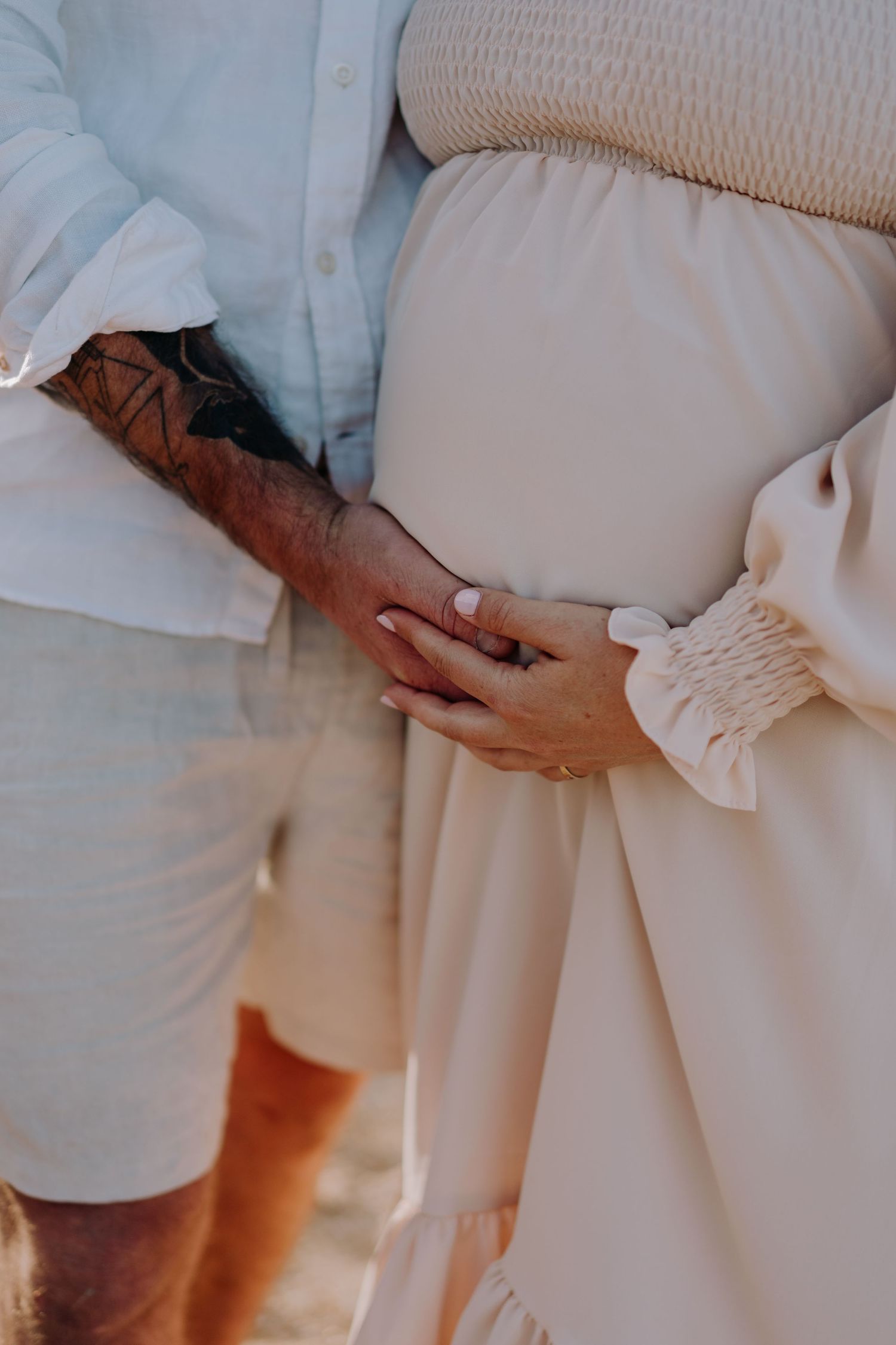 Close up of hands tenderly touching a pregnant belly in a white flowing dress.