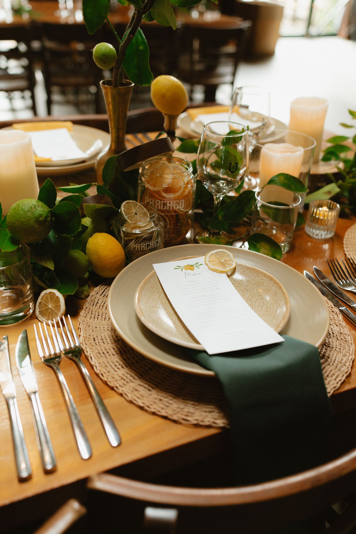 Citrus-themed wedding table setting with woven placemats and emerald green napkins.