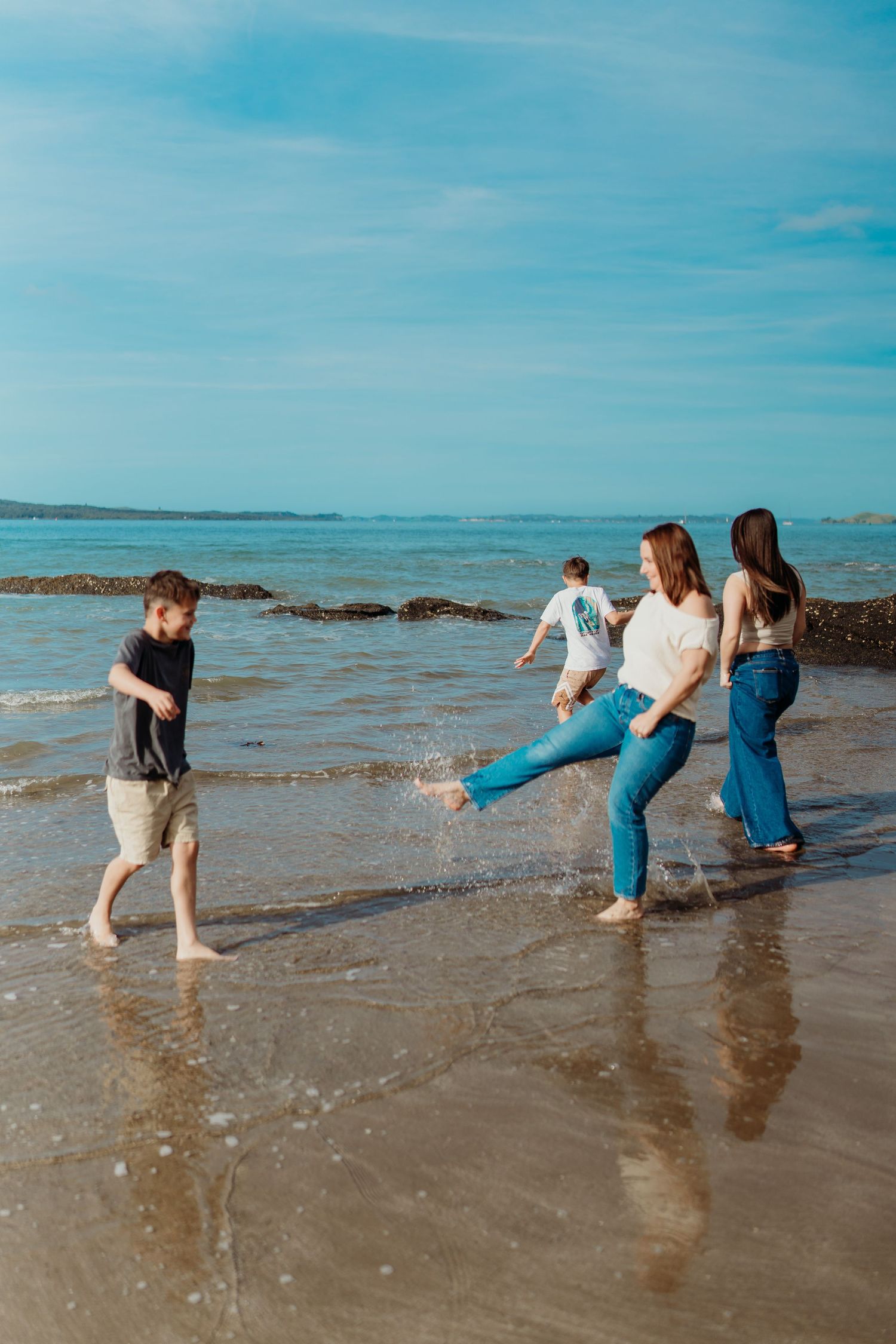 Family playing and splashing water on a sandy beach shore on a sunny day with blue skies.