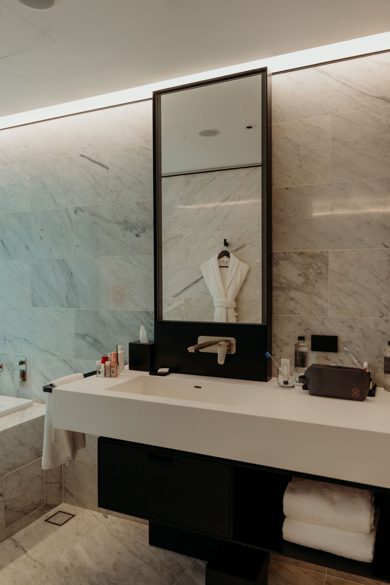 Modern luxury hotel bathroom with sleek marble walls, black accents, and minimalist design features.