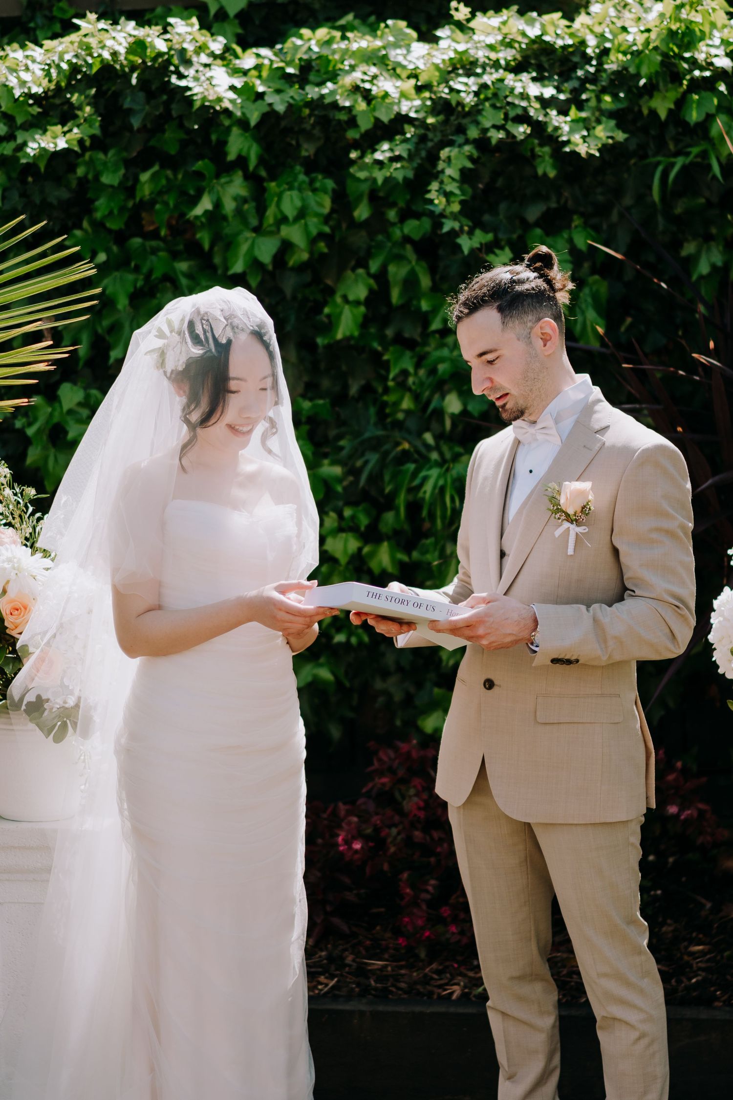 A wedding couple shares an intimate moment in front of flowering bushes and greenery.