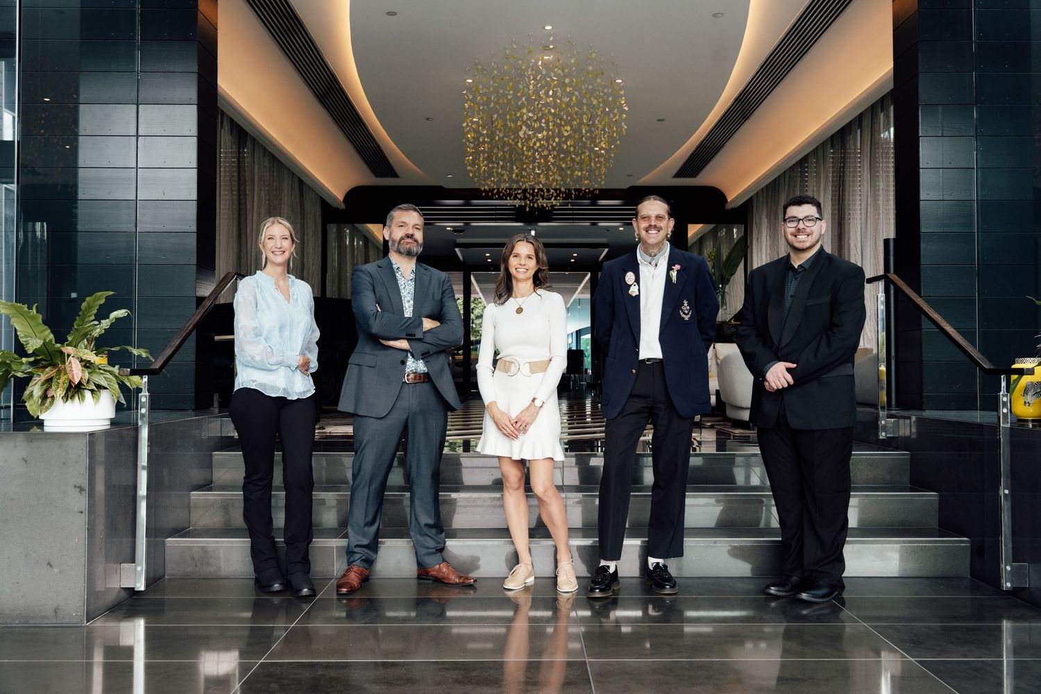 Five professionals posing together in a modern hotel lobby with chandelier and marble floors.