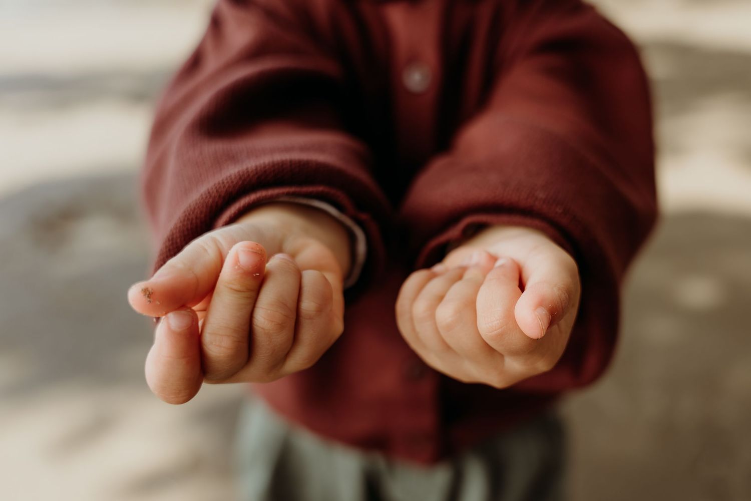 Close-up of a young child in a red hoodie extending both open hands forward in a giving or begging gesture.