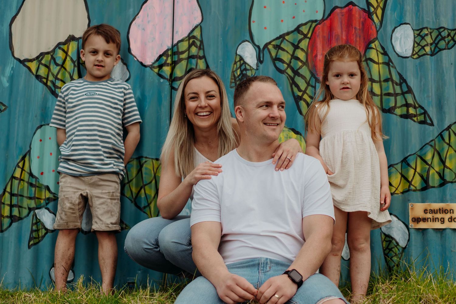 A family poses together in front of a vibrant turquoise wall decorated with green tree illustrations.