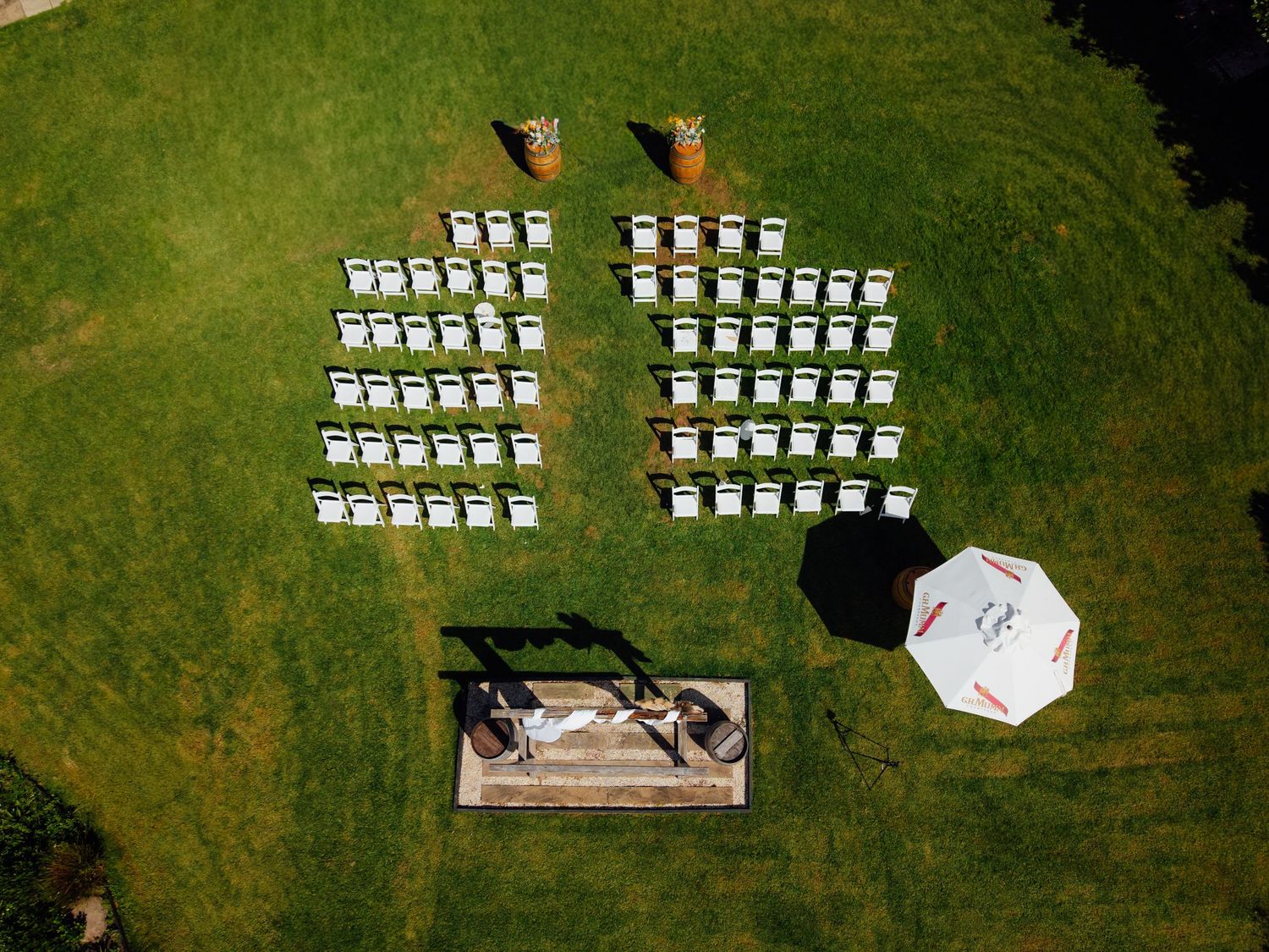 Aerial view of white chairs arranged in rows on green grass for an outdoor wedding ceremony with umbrella.