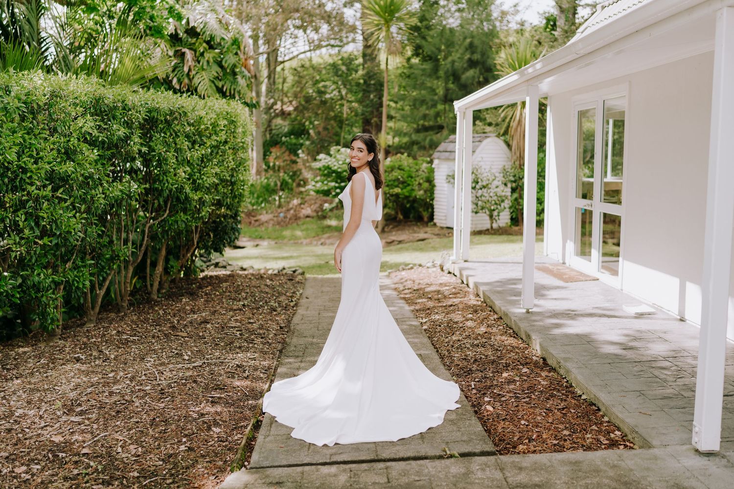 A white wedding dress silhouette against classic white columns and lush greenery.