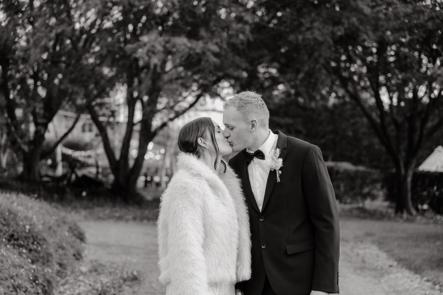 A romantic black and white outdoor wedding photo of a couple sharing a tender moment in a garden setting.
