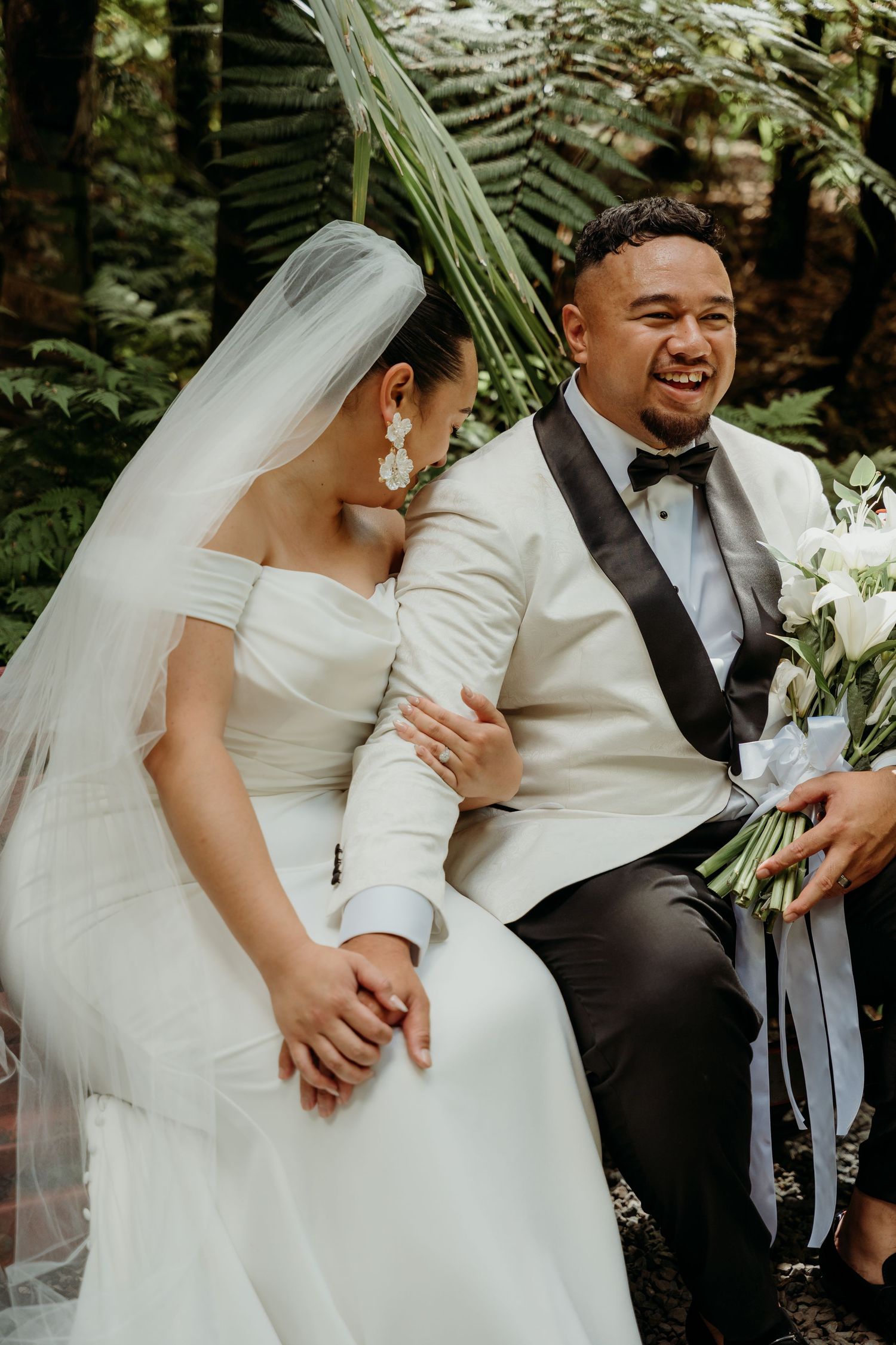 Joyful wedding moment captured in a garden setting with white attire and floral bouquet.