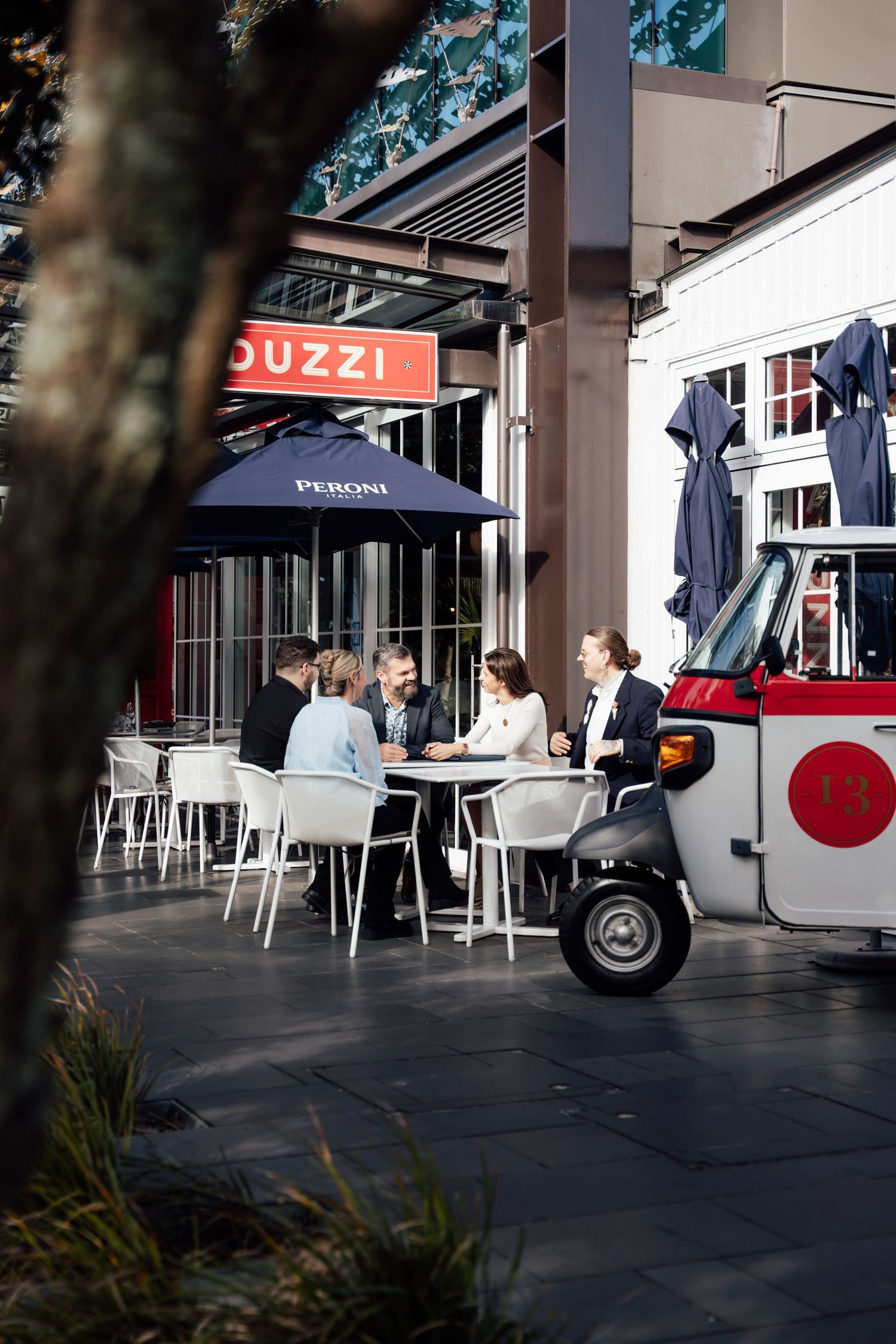 Business professionals meeting at outdoor cafe table under Peroni umbrella near Guzzi restaurant.