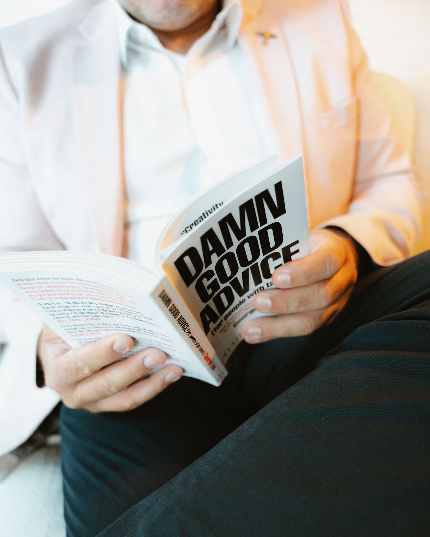 Man in blazer reading Damn Good Advice book, seated casually, close-up shot highlighting the bold title cover.
