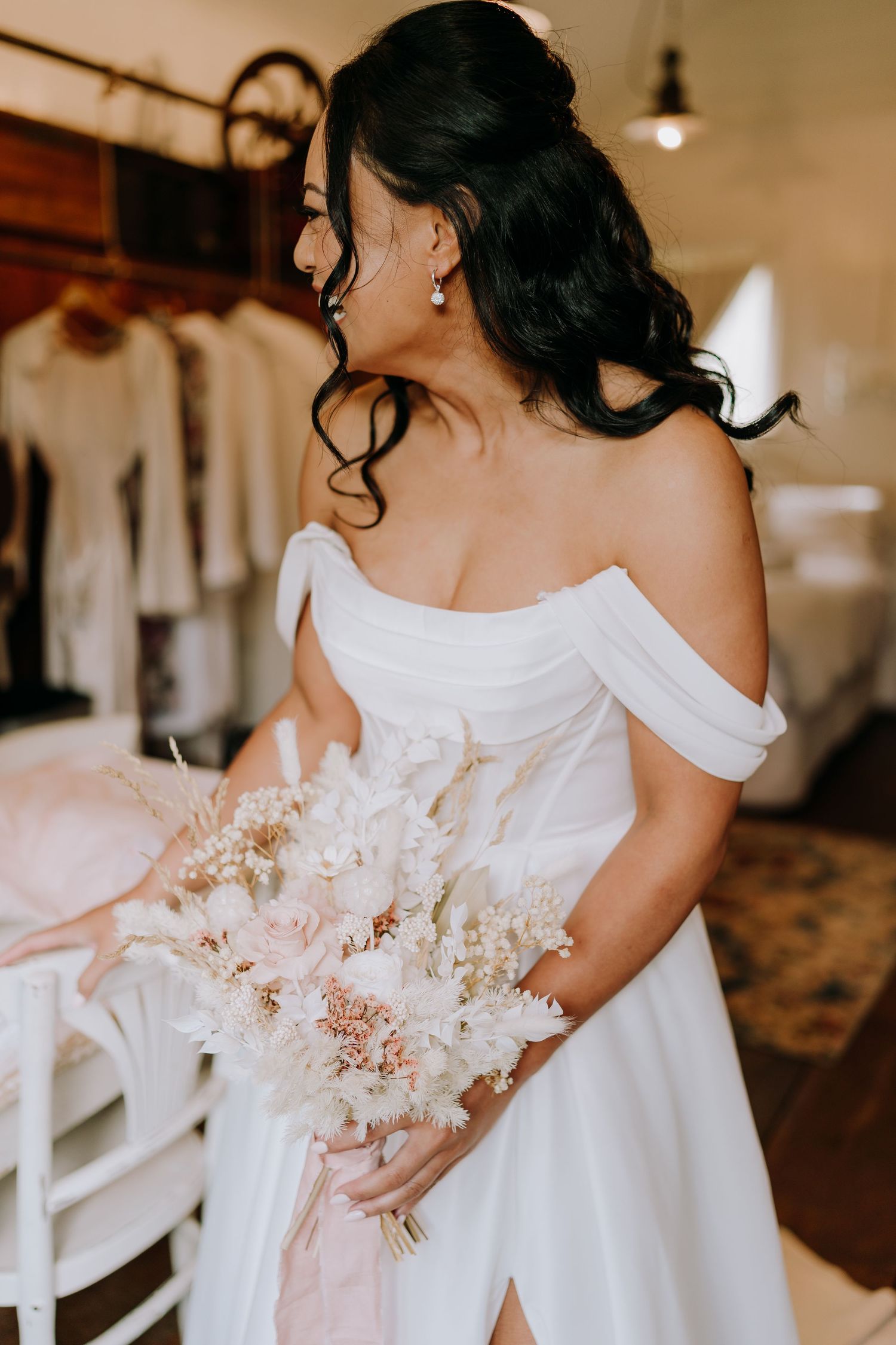 Bride in elegant off-shoulder white gown holds delicate pink and white bouquet.
