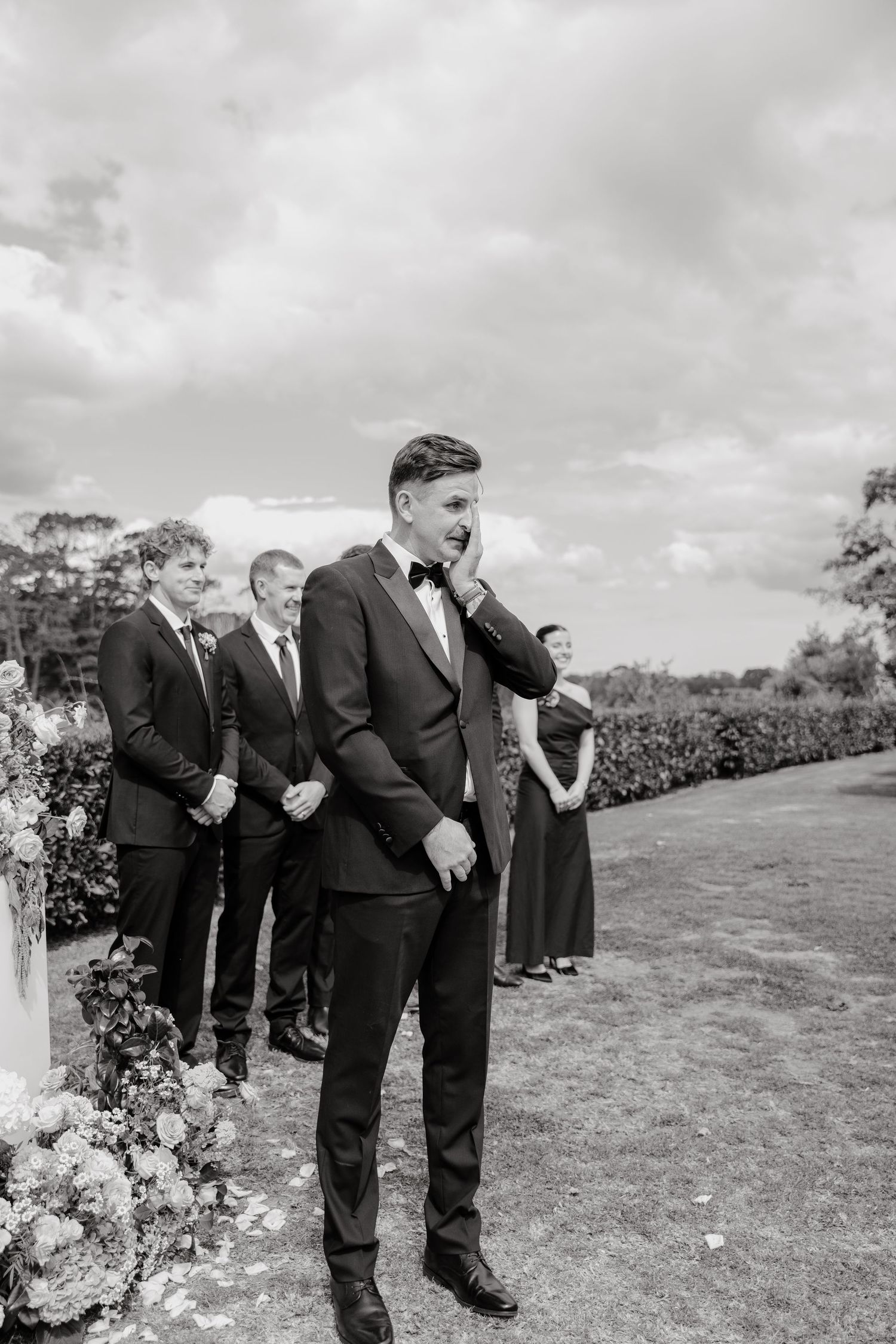 Wedding party members in formal attire gathered on a grassy hillside.