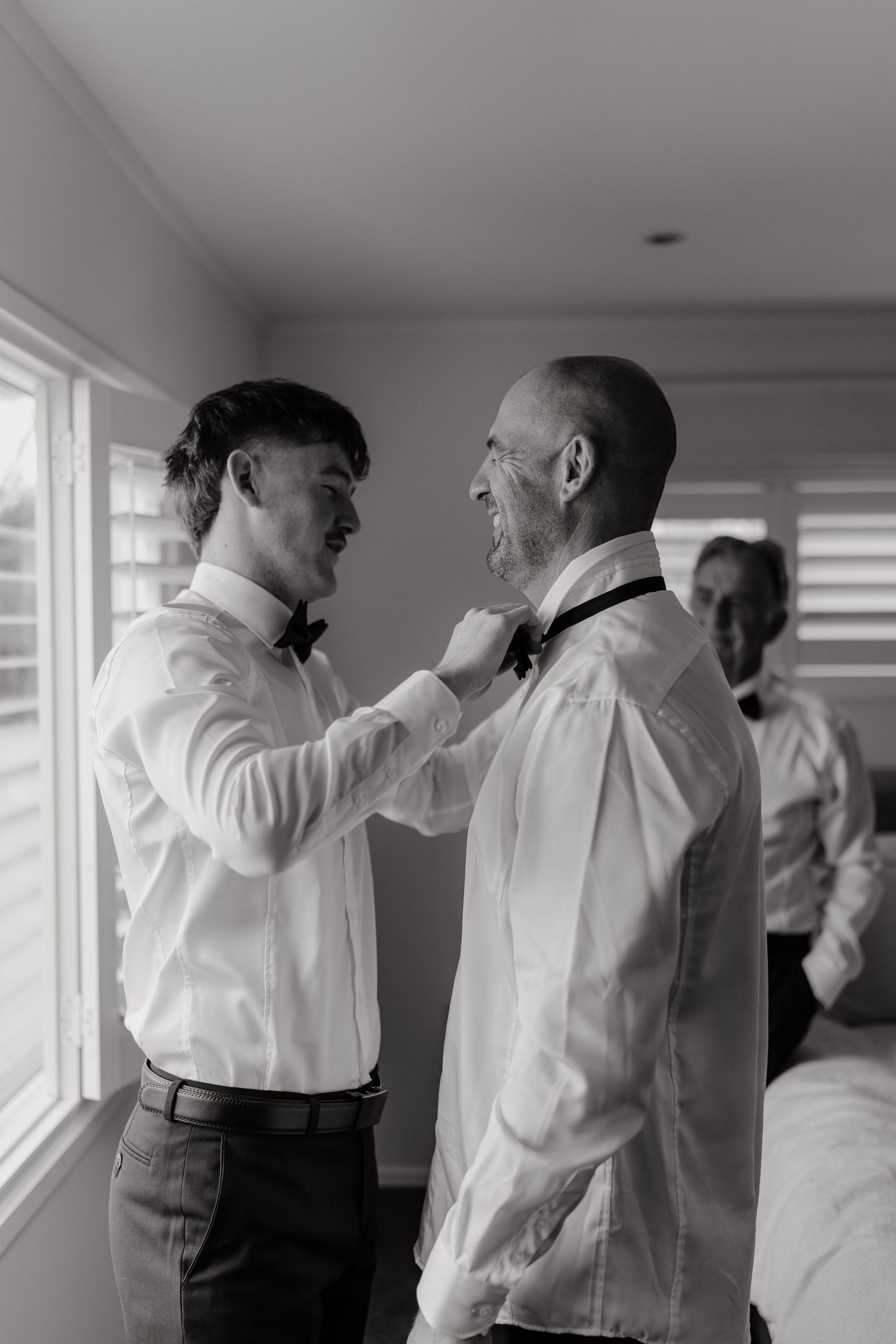 Black and white photo of groomsmen helping each other get ready before wedding ceremony.