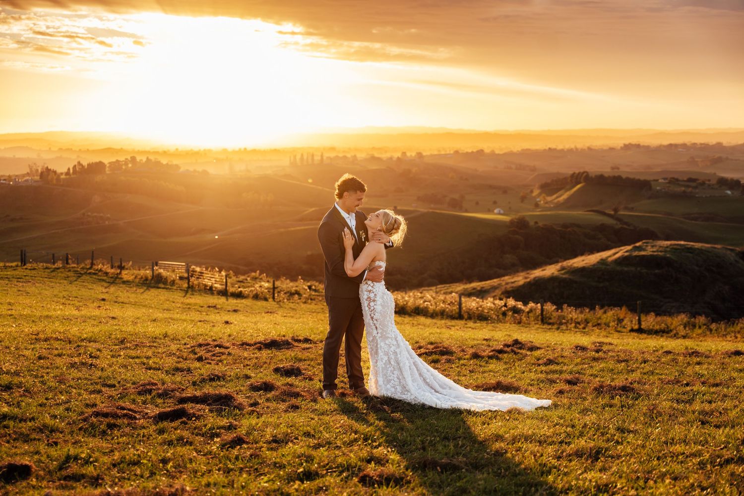 Romantic bride and groom embracing at golden sunset with rolling hills and vineyard in the background.