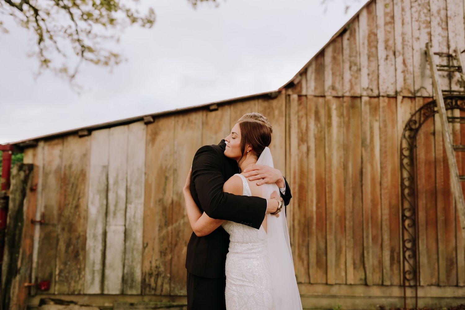 A couple embraces and dances together in front of a rustic wooden barn wall.