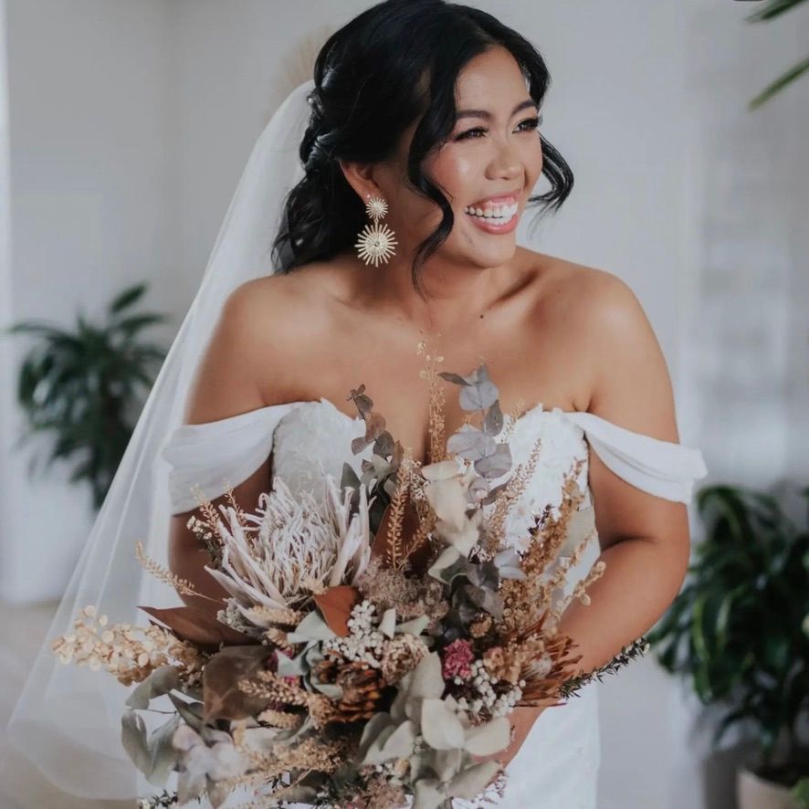 Bride in white wedding dress holds a beautiful dried floral bouquet with neutral tones and pampas grass.