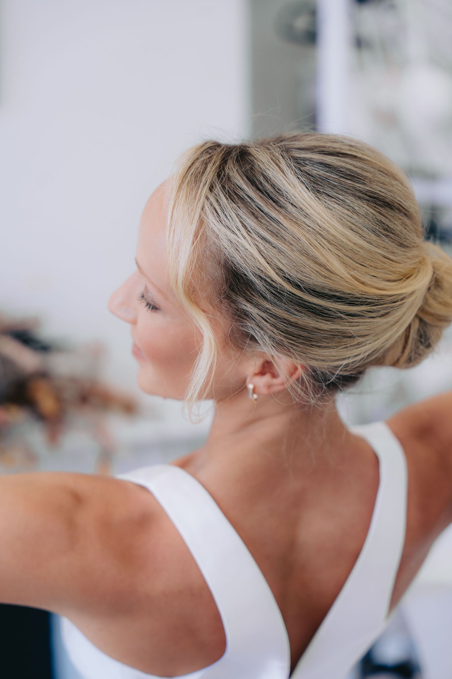Blonde woman with elegant updo hairstyle wearing a white dress, viewed from behind in a bright setting.