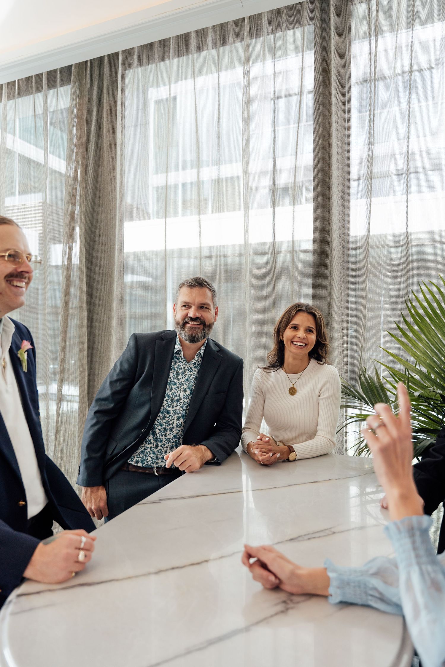 Business professionals smile during a meeting at a marble table in a modern conference room.