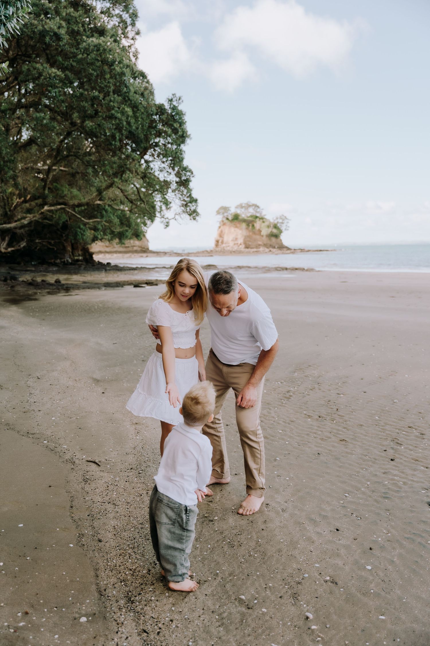 A group explores and plays together on a sandy beach with trees and ocean views in the background.