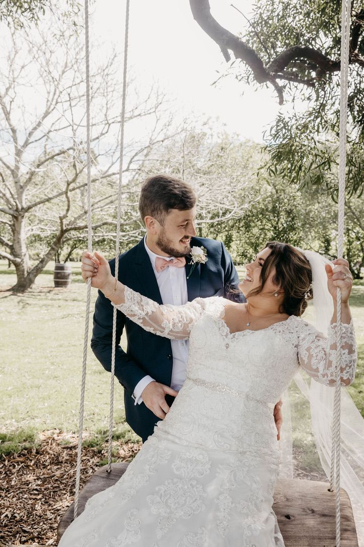 A couple shares a romantic dance together outdoors under trees, with the bride wearing a beautiful lace wedding dress.