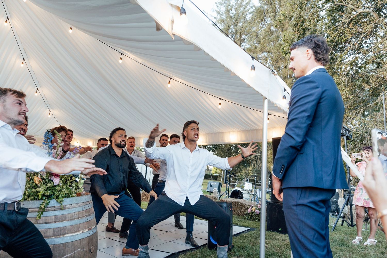 Men celebrating at an outdoor wedding reception under a white tent with string lights at dusk.
