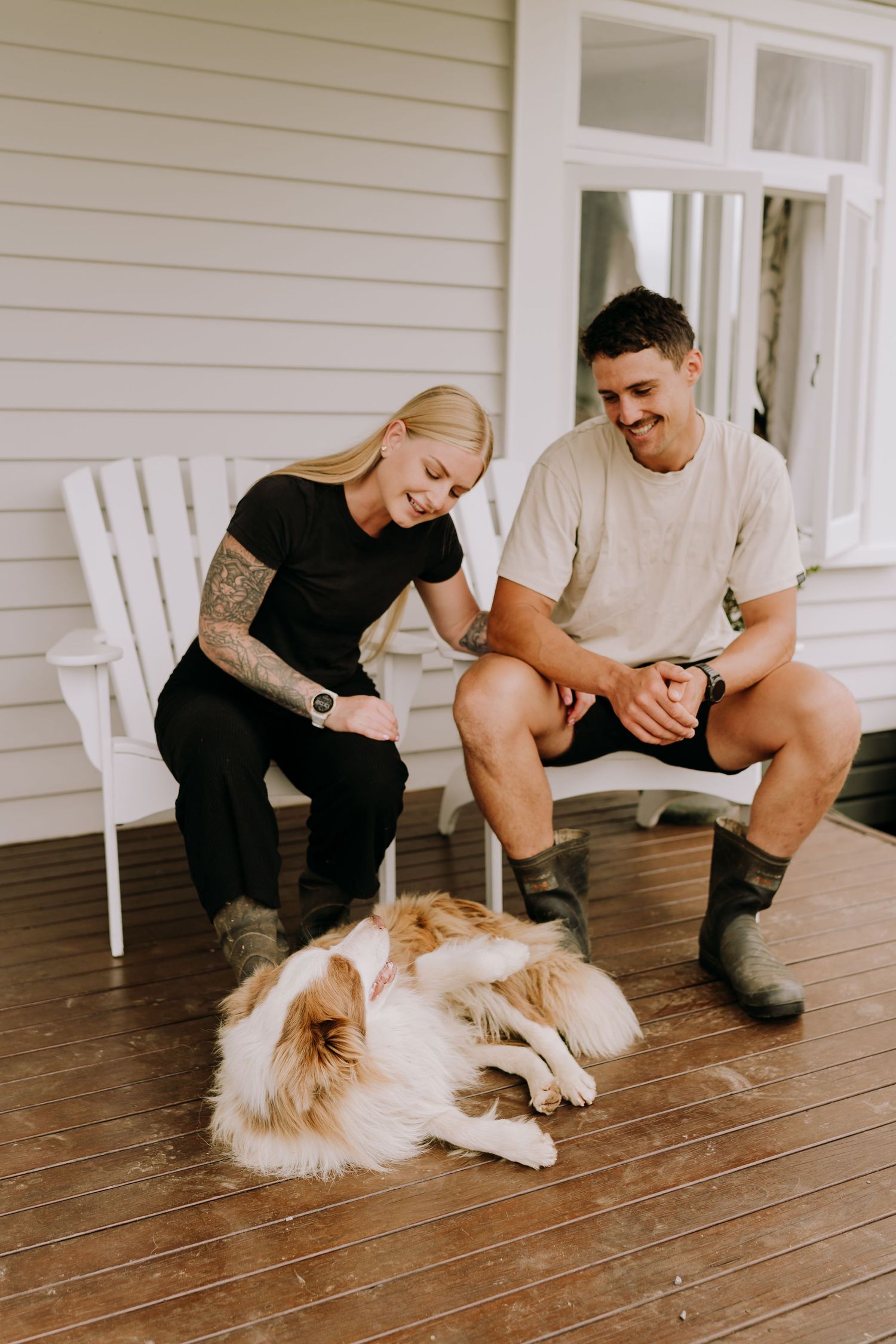 A couple relaxing on a white porch with their fluffy dog lying at their feet.
