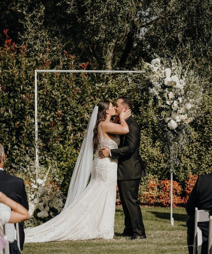 Romantic wedding couple shares intimate moments in a garden setting with flowing veil and natural greenery.