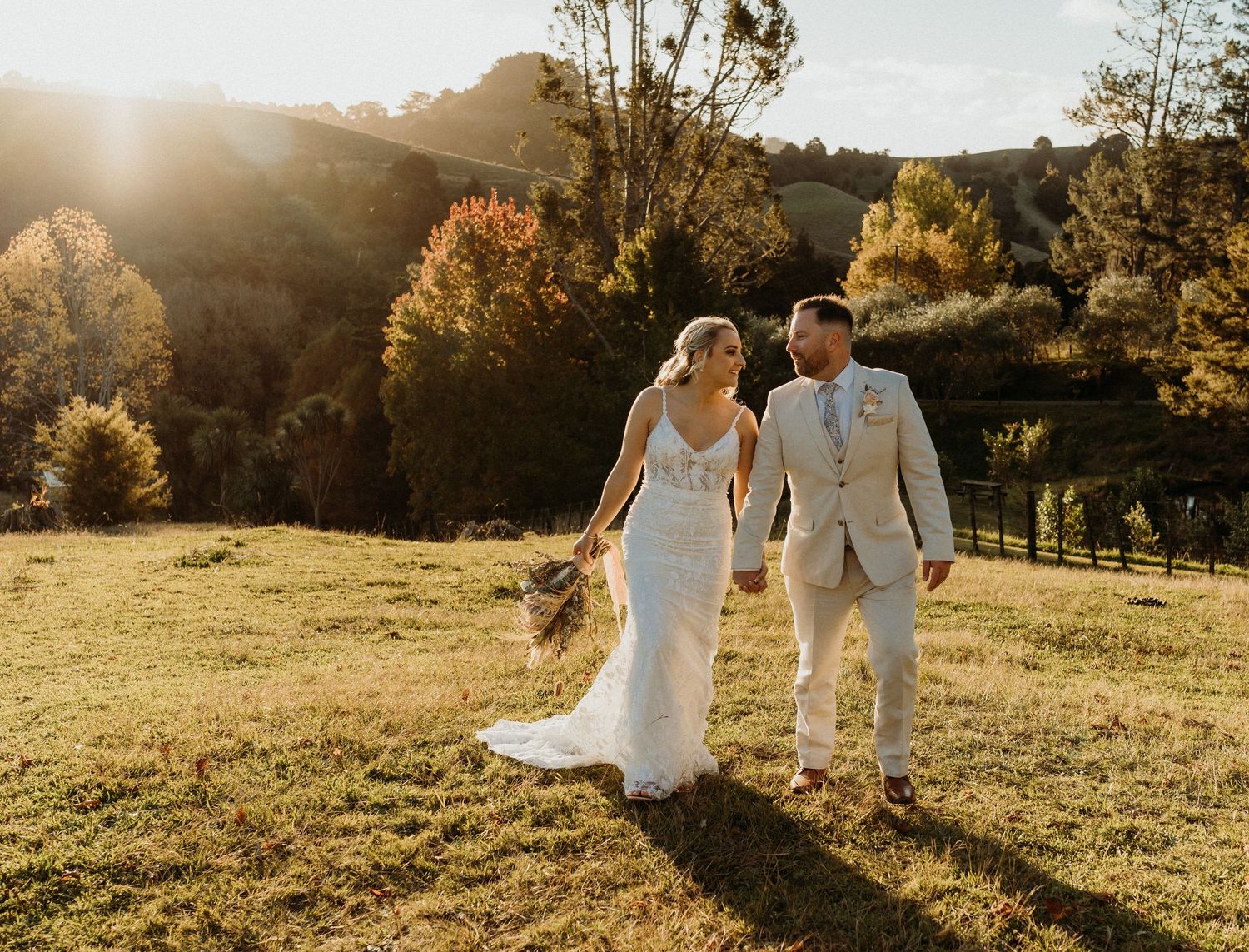 A couple walks hand in hand through a sunlit meadow at golden hour, their silhouettes casting long shadows on the grass.