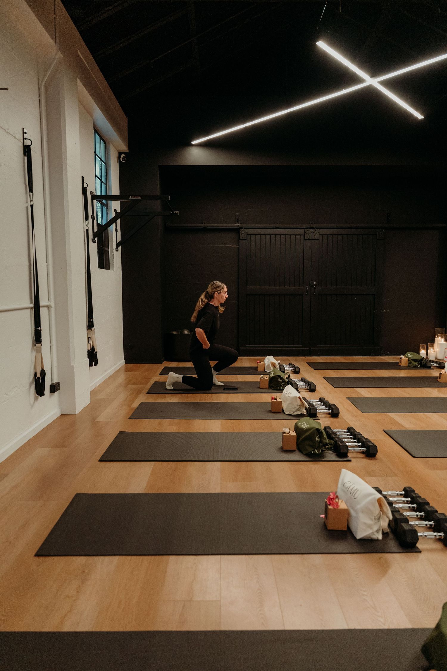 Woman practicing yoga lunge pose on black mat in modern fitness studio with wood floors and sleek lighting.