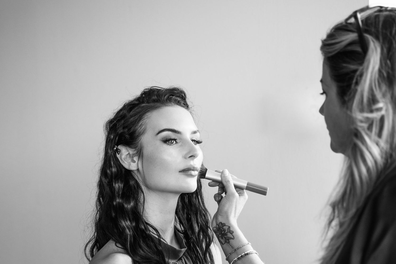 Black and white photo of a makeup artist applying lipstick to a young woman with curly hair.